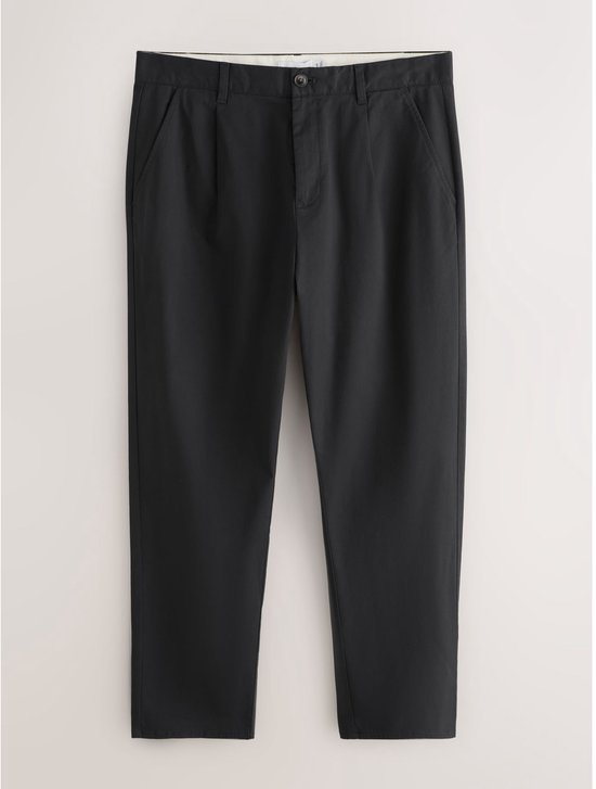 Zwarte chino broek met taps toelopende pijpen, platliggend tegen een lichte achtergrond.