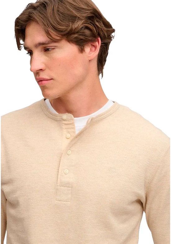 Close-up van het model in een beige waffle grandad-top met knoopsluiting en subtiel geborduurd logo.