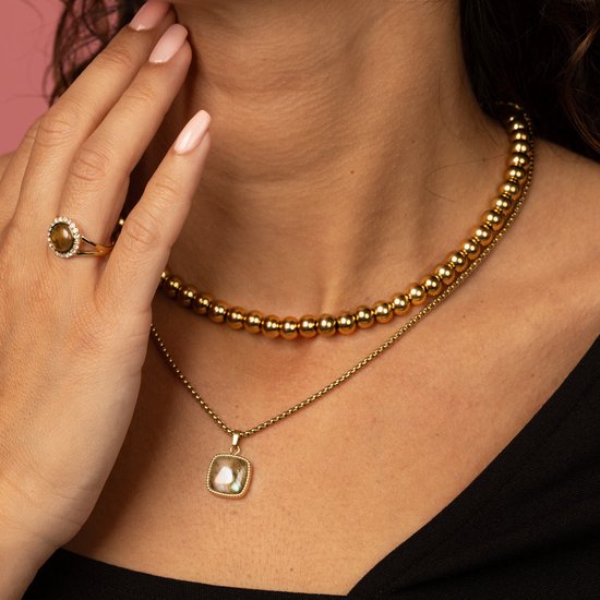 Vrouw met gouden kettingen met balletjes, een gouden ring met steen en een gedetailleerde hanger.