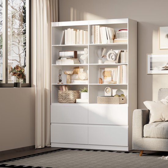 Wit boekenrek met open vakken en lades, naast een raam en een bank, met decoraties.