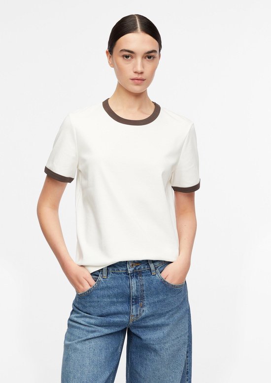 Model draagt wit T-shirt met bruine bies, handen in broekzakken.