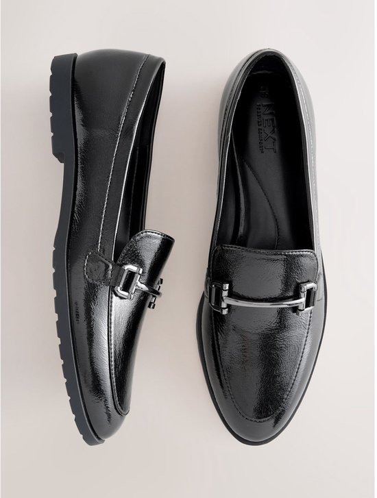Paar zwarte glanzende loafers met zilverkleurige gespen.