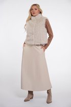 Model met lang blond haar, draagt een beige, langharige bontgilet, bruine coltrui en beige rok. Met de handen in de zakken.