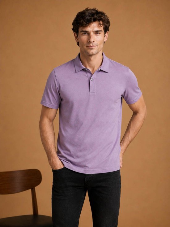 Een man met donker haar draagt een lavendelkleurig poloshirt met korte mouwen en zwarte jeans, handen in de zakken.
