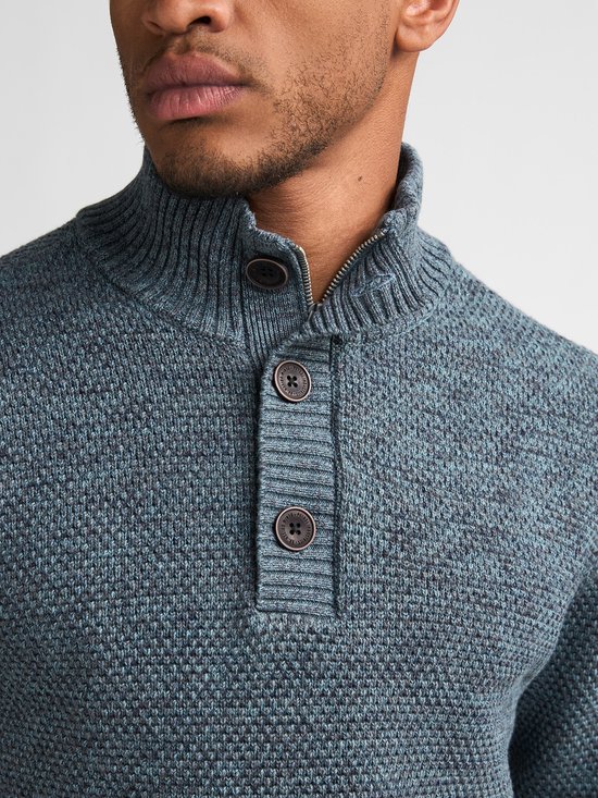 Detail van een blauwe gemêleerde sweater met hoge kraag, knoopsluiting en rits.