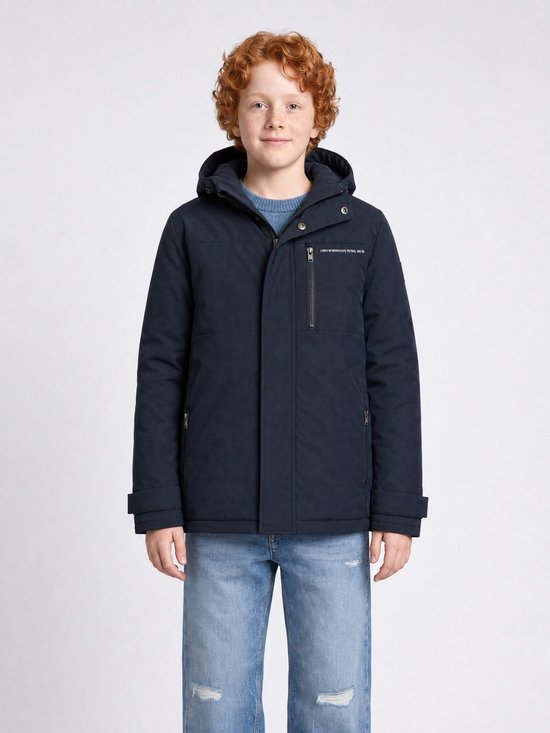 Jongen met krullend rood haar, draagt een donkerblauwe gewatteerde jas, blauwe trui en spijkerbroek.