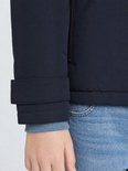 Detail van de mouw van een donkerblauwe jas, met opgestikte manchet en blauwe trui.
