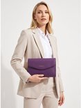 Vrouw in beige mantelpak met paarse clutch tas.
