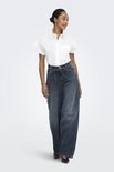 Model in een witte blouse en donkerblauwe wijde jeans met strikceintuur.
