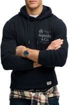 Model in donkerblauwe hoodie met gekruiste armen en geruit overhemd om middel.