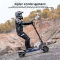 Man in motorkleding rijdt op een grijze elektrische scooter op een rotsachtig terrein.