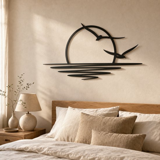 Décoration murale en métal noir d'un soleil couchant avec deux oiseaux en vol au-dessus des vagues, au-dessus d'un lit en bois.
