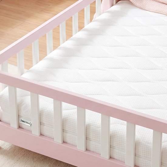 Witte matras met ruitpatroon en rits, geplaatst in een roze kinderhuisbedframe met witte spijlen.