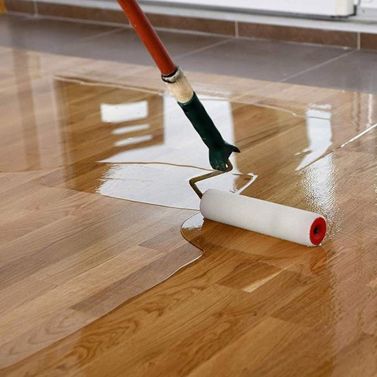 Roller brengt glanzende, kleurloze lak aan op een houten vloer.