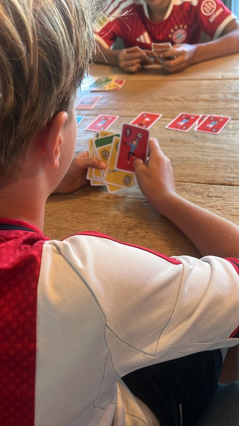 Jongen met blond haar houdt kaarten vast, met rode en witte voetbalshirts. Kaarten met voetbalmotieven zichtbaar.