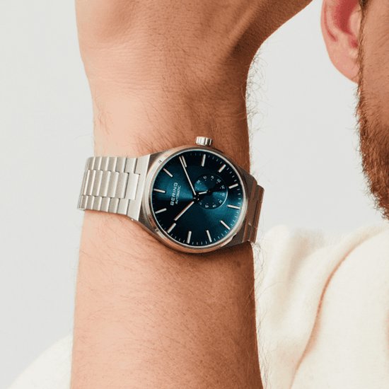 Zilverkleurig horloge met blauwe wijzerplaat en zilverkleurige band, gedragen om een pols. BERING AUTOMATIC.