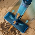 Serpillère électrique bleue avec réservoir d'eau et fonction de pulvérisation, montrant comment la saleté sur le plancher en bois est aspirée.