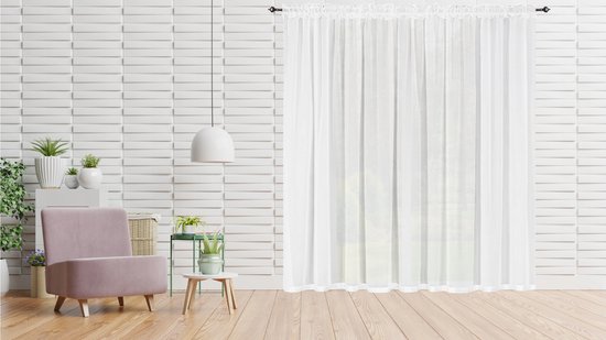 Witte doorschijnende vitrage gordijnen hangend voor een witte bakstenen muur met een roze fauteuil.