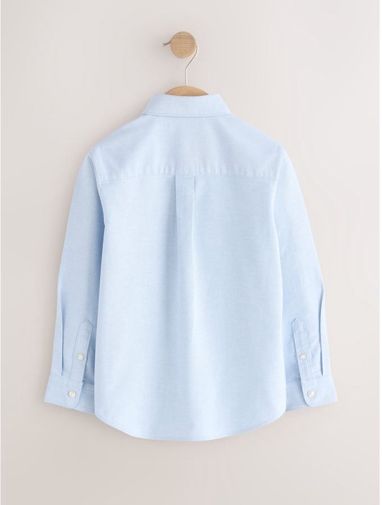 Achterkant van een lichtblauwe katoenen Oxford blouse met lange mouwen, hangend aan een houten kapstok.