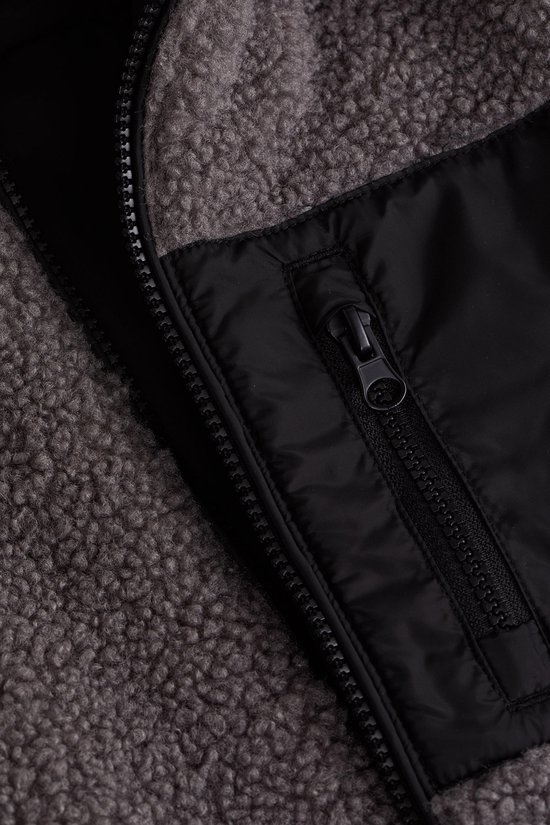 Sluiting van een grijze teddy jas met een zwart nylon borstvakje met rits.