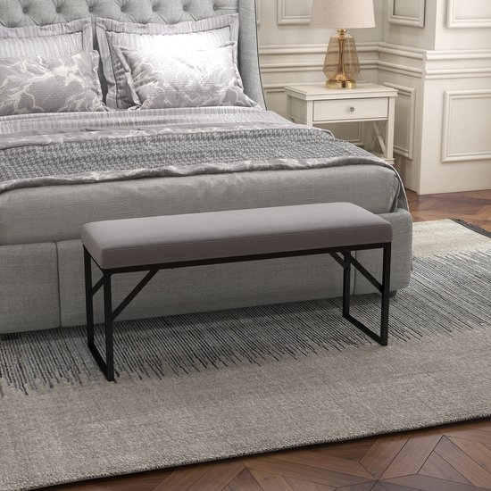 Grijze zitbank met zwarte metalen poten voor een bed met grijs gestoffeerd hoofdeinde.