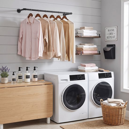 Een zwarte kledingstang met lichte kleding boven twee wasmachines in een moderne wasruimte.