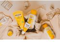 WELEDA Baby producten met oranje en gele accenten, waaronder een tube shampoo, een tube billenbalsem en een flesje verzorgende olie.