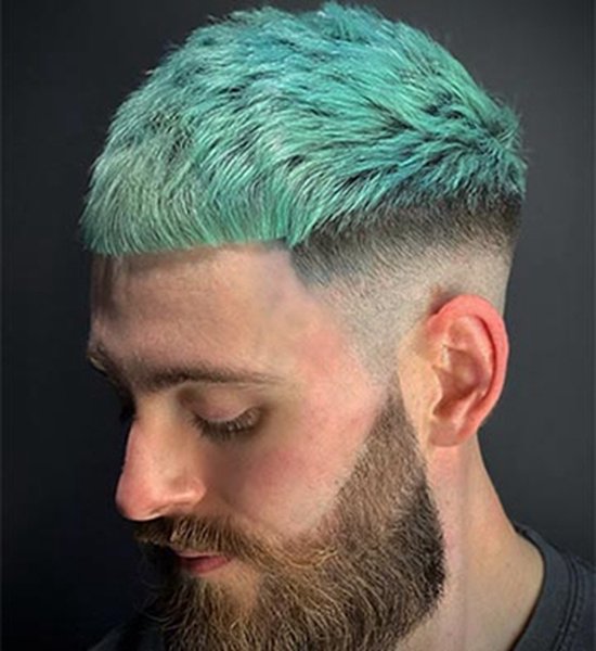Man met kort, geföhnd, fel blauwgroen haar en een geschoren baard.