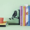 Zwarte boekensteun met uil op tak, naast boeken en een oranje doosje.