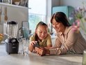 Moeder en dochter kijken naar een smartphone naast een zwarte Philips blender met glazen kan en drinkglazen.