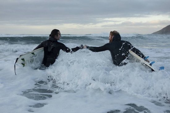 Twee mannen met surfplanken in woelige zee, geven elkaar een vuistje.