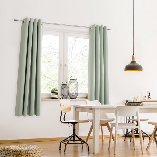 Twee zachtgroene verduisterende gordijnen hangen voor een raam in een eethoek met een witte tafel en stoelen.