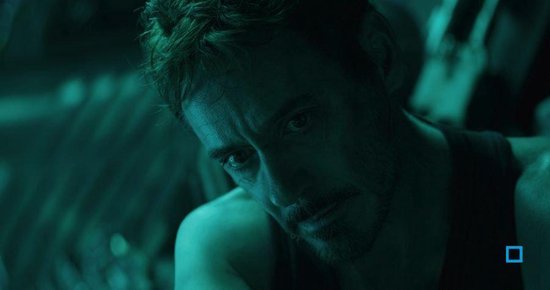 Close-up van Tony Stark (Iron Man) met een groene gloed over zijn gezicht, kijkend naar beneden.