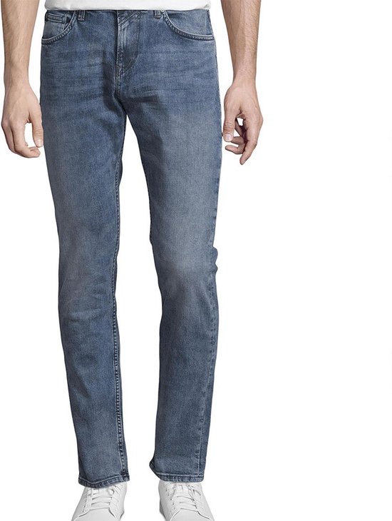 Man met witte t-shirt en blauwe jeans, staand, recht van voren gefotografeerd.