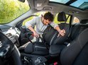 Man stofzuigt autostoel met rode slang en grijze stofzuiger.