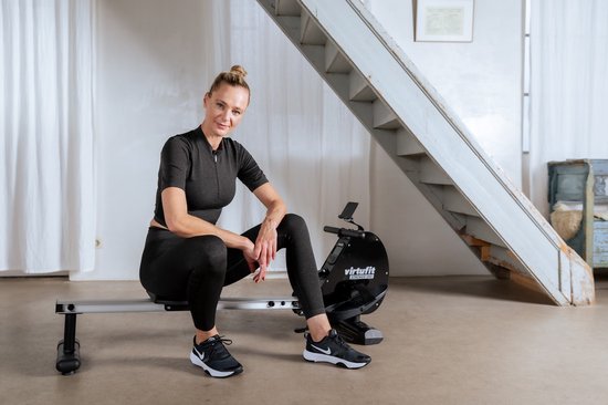 Een vrouw met blonde paardenstaart, gekleed in zwart, zit op de VirtuFit roeimachine.
