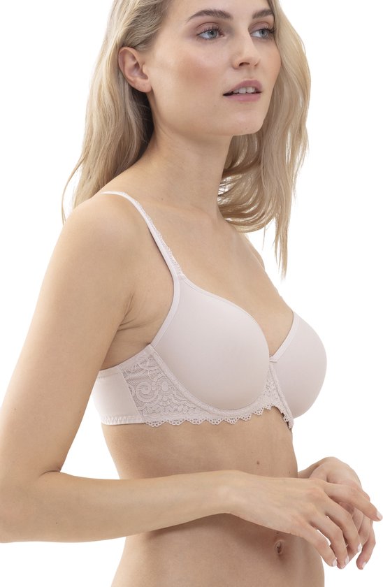 Une femme aux cheveux blonds, portant un soutien-gorge beige avec des détails en dentelle sur les bonnets et les bretelles.