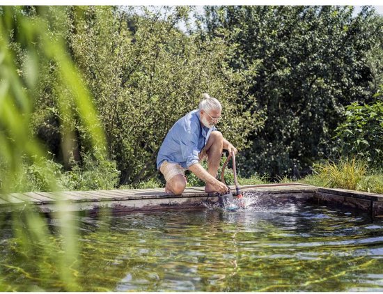 Man met grijs haar knielt bij een vijver en gebruikt een vuilwaterpomp.