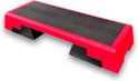 Een rood aerobic step met een zwart anti-slip oppervlak en verstelbare pootjes voor verschillende hoogtes.