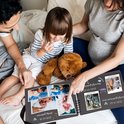 Een familie met een baby, een jong kind en een zwangere vrouw bekijkt een fotoalbum met babyfoto's. Een teddybeer ligt tussen hen in.