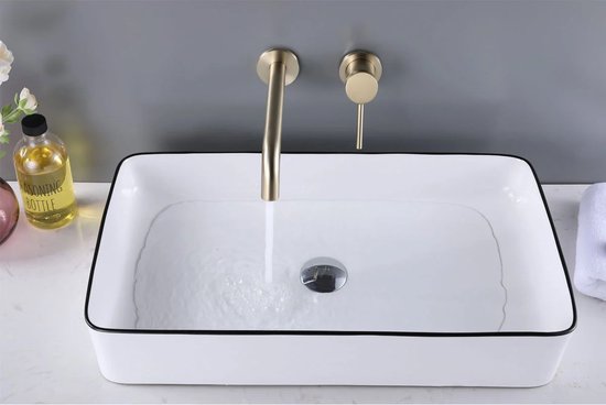 Mat gouden inbouwkraan boven een rechthoekige witte wasbak met zwarte rand. Water stroomt.