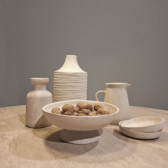 Een groep decoratieve aardewerk objecten in off-white, waaronder vazen, kommen, en een schenkkan, op een marmeren tafel.