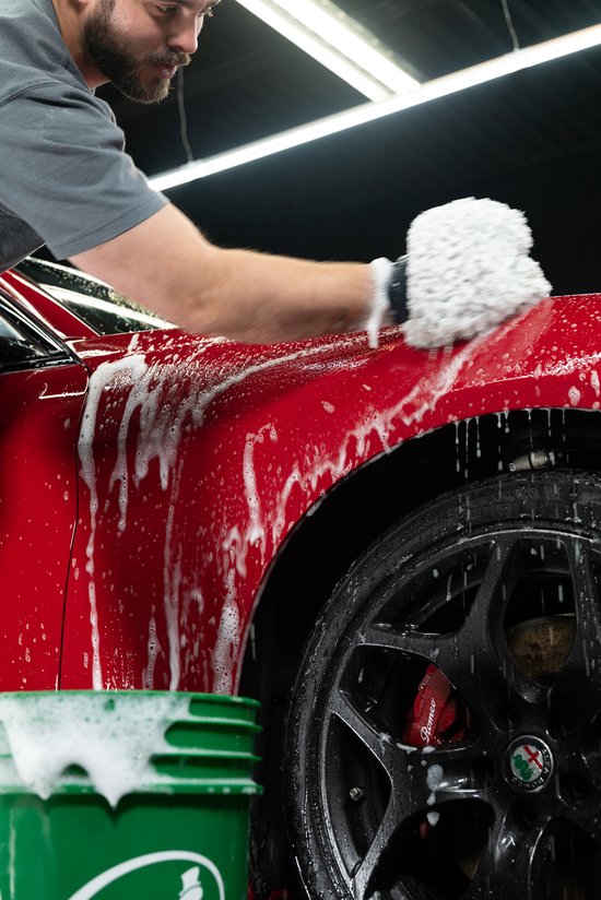 Man wast rode auto met schuimende shampoo en spons. Close-up op voorwiel en spatbord.