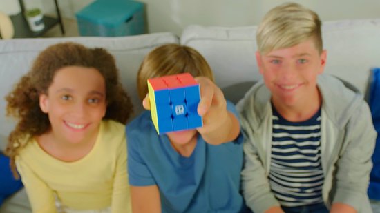 Een jongen houdt een blauw-rood-gele kubus voor de camera. Twee meisjes en een jongen kijken lachend mee.