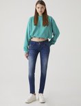 Model met lang bruin haar in blauwe jeans met knoopsluiting.
