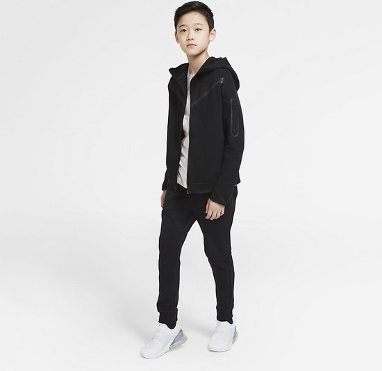 Jongen poseert in een zwarte Nike Tech Fleece hoodie en broek.
