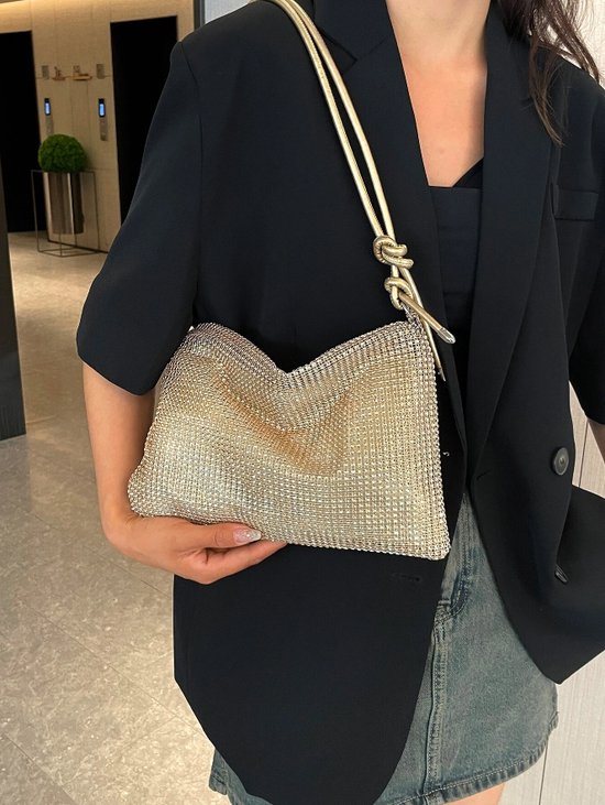 Gouden metallic clutch met zilverkleurige versieringen en een goudkleurige band, gedragen door een model.