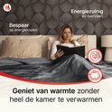 Vrouw leest boek onder een grijze elektrische deken, bespaart op energiekosten. Geniet van warmte zonder de hele kamer te verwarmen.