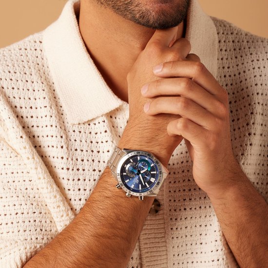 Herenhorloge met zilverkleurige metalen band en blauwe wijzerplaat, gedragen door een model in een crèmekleurige gebreide cardigan.