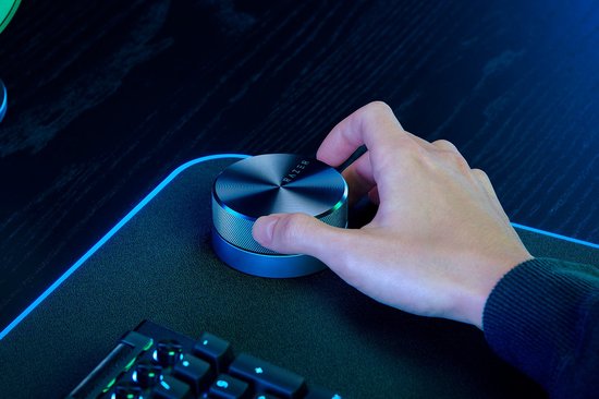 Hand draait aan Razer volume knop op gaming bureau.